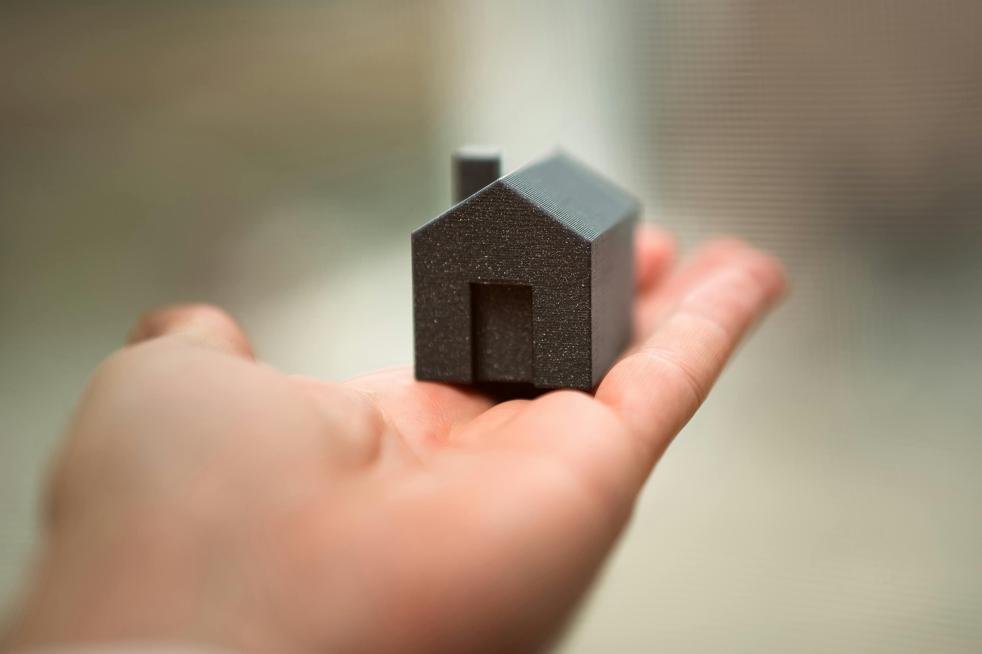 Hand hält ein kleines Hausmodell als Symbol für die Entscheidung zwischen Kauf und Miete